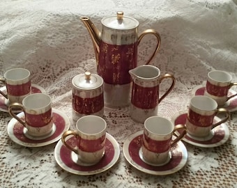 May include: A vintage porcelain tea set with gold accents. The set includes a teapot, creamer, sugar bowl, and six cups and saucers. The cups and saucers feature a burgundy and gold floral pattern.