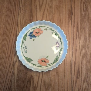 May include: A white ceramic baking dish with a scalloped edge and a floral design featuring pink, blue, and green poppies.