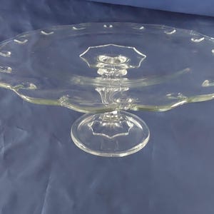 May include: A clear glass cake stand with a scalloped edge and a pedestal base.