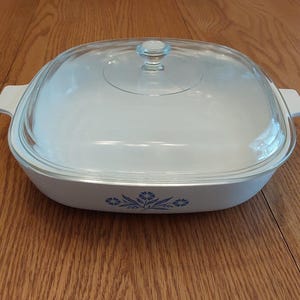 A White Corningware square handled 10 inch casserole dish P-10-B in the blue cornflower design with matching clear lid P-10-C.  CD 314