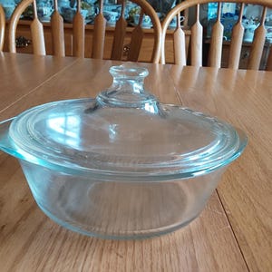 A round Glasbake clear glass 1 quart bowl with handles that has a matching lid with center knob handle, microwave & dishwasher safe.  CD 298