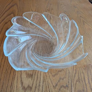 May include: A clear glass serving bowl with a spiral design. The bowl has a unique shape with curved edges and a central swirl pattern. The bowl is made of transparent glass and is suitable for serving snacks or displaying decorative items.