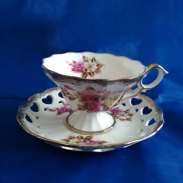 A Ucagco Ceramics white matching pedestal cup and saucer in, with white and pink roses, gold trimwith open heart lace. CS 342