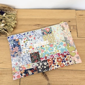 Peut inclure: Une pochette en tissu patchwork avec une fermeture éclair dorée. La pochette est composée de divers tissus à motifs floraux dans les tons de bleu, rose, rouge et blanc. Le texte "TETE DE NINOTTE" est imprimé sur une petite étiquette.