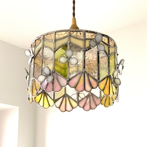 Puede incluir: Una lámpara de techo de cristal de colores con un diseño floral. La luz presenta una variedad de colores, incluyendo rosa, amarillo y verde. Las flores están hechas de cristal de colores y están dispuestas en un patrón circular.