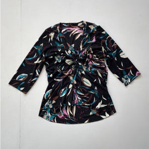 May include: Black three-quarter sleeve top with a V-neck and a gathered knot detail at the waist. The top features a floral pattern in teal, pink, brown, and white. The fabric appears to be a soft, flowing material.