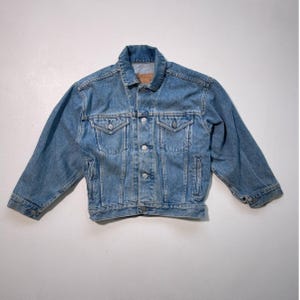 May include: Light blue denim jacket with a classic collar, button-down front, and two chest pockets. The jacket has long sleeves and a slightly faded appearance, suggesting a vintage or worn look. The jacket is a standard fit.