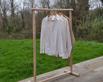 Perchero de madera natural, expositor de madera en bruto, perchero minimalista de madera clara, para tiendas conceptuales y salas de exposición.