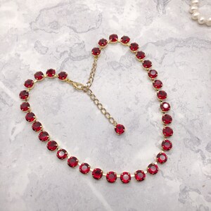 May include: A gold chain necklace with a row of red round rhinestones. The necklace has an adjustable clasp.