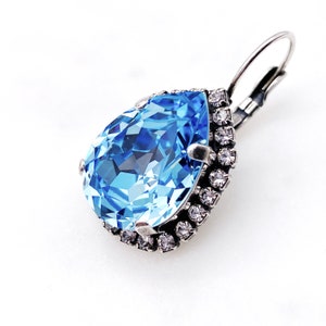 May include: A teardrop-shaped blue crystal earring with a silver setting and a halo of smaller clear crystals.