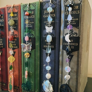 May include: Five bookends with different colored beads and charms hanging from them. The bookends are all made of metal and have a silver finish. The beads are all different colors and shapes, and the charms are all different designs. The bookends are all attached to books with the title "Junior Classics" on the spines.