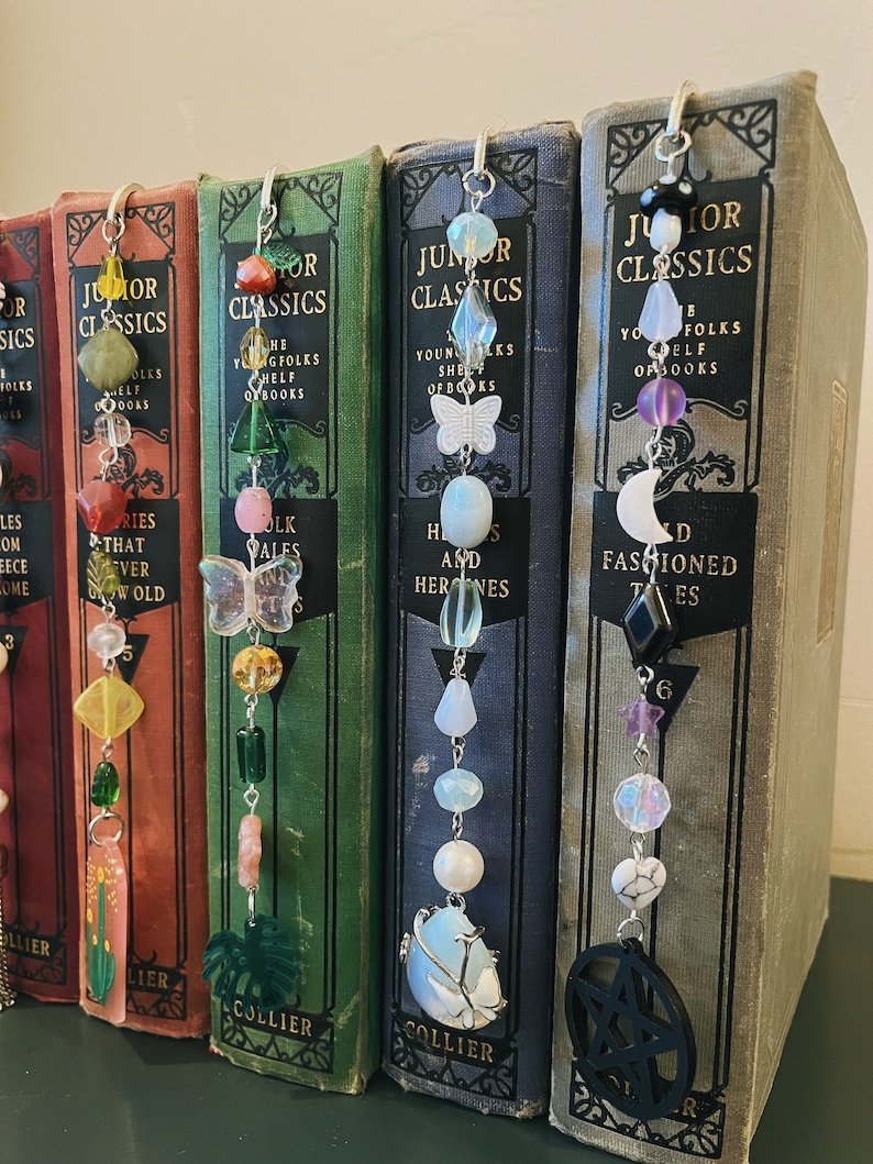 May include: Five bookends with different colored beads and charms hanging from them. The bookends are all made of metal and have a silver finish. The beads are all different colors and shapes, and the charms are all different designs. The bookends are all attached to books with the title "Junior Classics" on the spines.