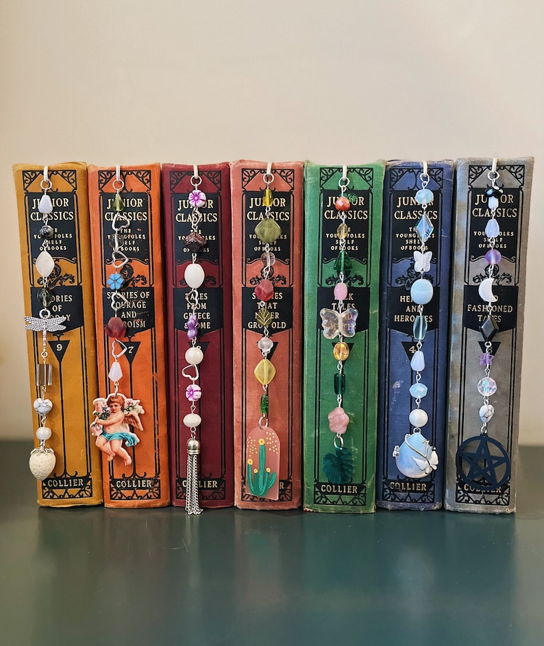 May include: A set of ten colorful beaded bookmarks with charms, each attached to a vintage book with the title "Junior Classics". The charms include a butterfly, a flower, a star, a cactus, a dragonfly, a heart, a crescent moon, a pentagram, a tassel, and a cherub.