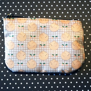 May include: A small, beige zippered pouch with a checkered pattern featuring cartoon bunnies. The pouch is made of a soft, fabric material.
