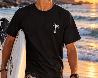 Könnte beinhalten: Ein schwarzes kurzärmeliges T-Shirt mit einer kleinen weißen Palmen-Grafik auf der linken Brust, kombiniert mit einer schwarzen Shorts mit hellem Blattmuster und einem weißen Surfbrett mit schwarzen Akzenten an der Seite.