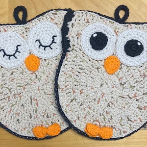 May include: Two crocheted owl pot holders. One owl has black eyes and the other has closed eyes with eyelashes. Both owls have orange beaks and feet.