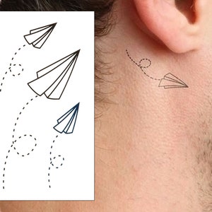 以下が含まれることがあります： 3つの黒いアウトラインの紙飛行機のデザインが描かれた一時的なタトゥーのシート。各飛行機は、飛行を示唆する点線があります。