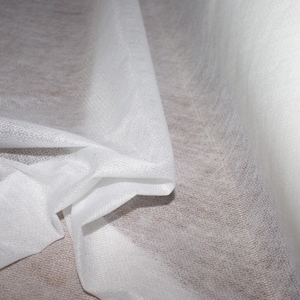 May include: White sheer fabric with a slightly textured surface. The fabric is folded and draped, creating soft folds and curves.