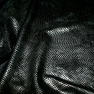 May include: Black textured fabric with a snakeskin pattern. The fabric is draped and folded, creating a textured background.