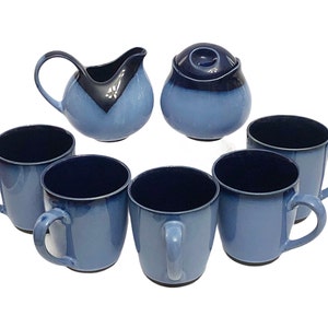 May include: A set of six blue ceramic mugs with black rims and a matching creamer and sugar bowl. The mugs have a gradient blue color with a darker blue rim.