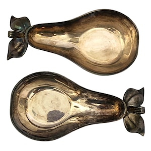 Op de afbeelding: Twee zilverkleurige, peervormige serveerschalen. Elke schaal heeft een diepe, ovale kom en een decoratief blad- en steeldessin aan de bovenkant. De schalen staan tegen een witte achtergrond.