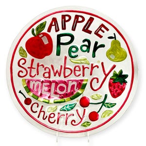 Può includere: Un piatto decorativo rotondo in vetro trasparente con illustrazioni di frutta dipinte e testo. Il design include una mela rossa, una pera verde, una fragola, una fetta di anguria e ciliegie, con le parole Apple, Pear, Strawberry, Melon e Cherry.
