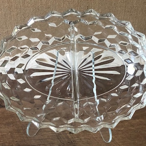 Puede incluir: Un plato de servir de vidrio transparente dividido con un patrón de diamante. El plato tiene dos secciones ovaladas y un divisor central elevado.