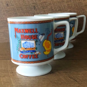 Könnte beinhalten: Set aus drei weißen Keramik-Kaffeetassen mit einem blauen und roten Maxwell House Kaffeelogo. Die Tassen haben einen Sockel und einen Henkel.