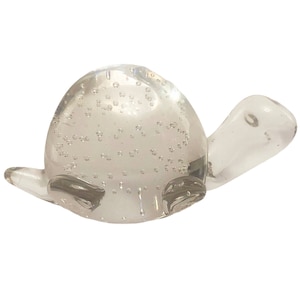 Puede incluir: Una figurita de tortuga de vidrio transparente con burbujas de aire en todo el cuerpo. La tortuga está sentada sobre un fondo blanco.