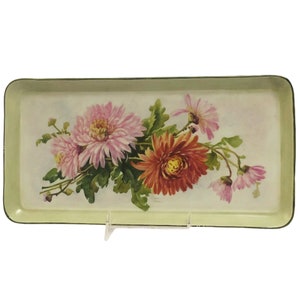 May include: A vintage metal tray with a green rim and a white background. The tray features a floral design with pink, red, and white flowers.