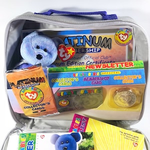 Könnte beinhalten: Eine graue Reißverschlusstasche mit einem blauen Griff. Die Tasche ist geöffnet und enthält einen blauen Beanie Baby, ein Zertifikat, eine Mitgliedskarte, eine Sammlermünze und eine Sammlerkarte. Der Text auf dem Zertifikat lautet "Platinum Membership Beanie Babies Official Club™ Platinum Edition Certificate".