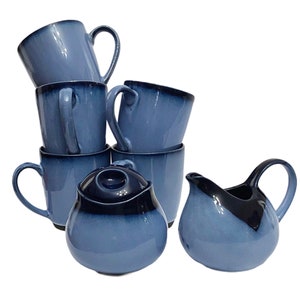 Może przedstawiać: Zestaw sześciu niebieskich i czarnych ceramicznych kubków z pasującym dzbankiem do mleka i cukiernicą. Kubki mają gradientowy wzór z ciemniejszym niebieskim u góry i jaśniejszym niebieskim u dołu. Dzbanek do mleka i cukiernica mają podobny wzór.