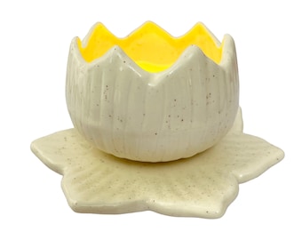 May include: A white ceramic planter shaped like a lotus flower with a yellow glazed interior. The planter sits on a matching white ceramic base.