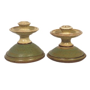 May include: A pair of ceramic candle holders with a green base and a cream colored top. The candle holders have a simple, elegant design.