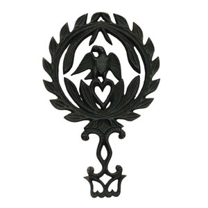 May include: Black cast iron trivet with a bird and heart design in a wreath of leaves. The trivet has a decorative base.