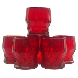 Puede incluir: Conjunto de cinco vasos de vidrio rojo con un diseño texturizado y facetado. Los vasos están apilados en forma de pirámide.