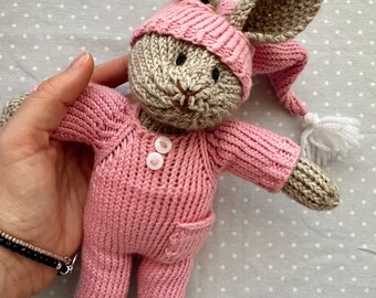 May include: A knitted pink bunny wearing a pink and white sleep cap. The bunny has brown ears and a brown face with black eyes.