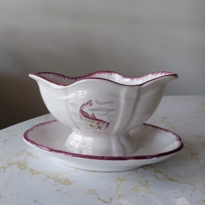 May include: White ceramic gravy boat with a burgundy rim and a painted fish design. The boat is on a matching saucer.