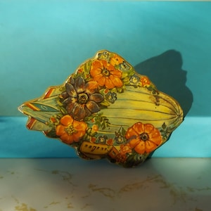 May include: A vintage, hand-painted, paperweight shaped like a blimp with floral details. The blimp is painted in shades of blue, yellow, and green, with orange and purple flowers.