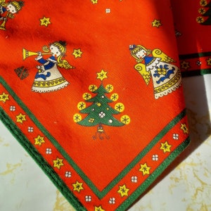 Può includere: Tessuto rosso con bordo verde e un motivo ripetitivo di angeli che suonano la tromba, alberi di Natale e stelle. Il tessuto ha un tema natalizio festoso.