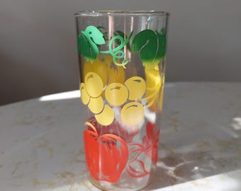 Könnte beinhalten: Ein klares Glas mit einem Fruchtdesign. Das Glas zeigt gelbe Trauben, einen roten Apfel und grüne Blätter. Das Design ist auf der Außenseite des Glases aufgedruckt, das zylindrisch geformt ist.