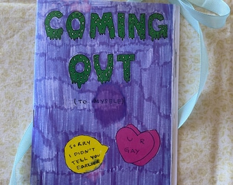 May include: A purple and green illustrated book with the title "Coming Out (To Myself)". The book has a yellow speech bubble that says "Sorry I didn't tell you earlier" and a pink heart that says "Ur Gay".