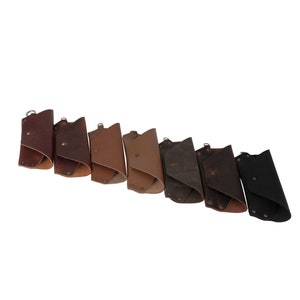 May include: Seven leather keychains in various shades of brown, from light to dark, with a black keychain at the end. Each keychain has a metal ring and is folded in half.