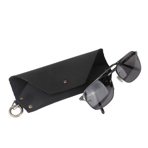 May include: Black leather sunglasses case with a metal clasp and a pair of black sunglasses with silver frames.