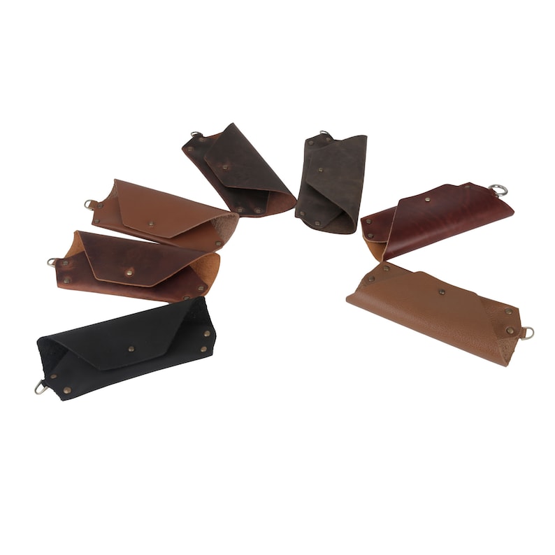 May include: Assortment of eight leather keychains in various colors, including brown, black, and tan. Each keychain has a metal ring and a folded leather design.