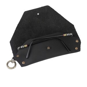 May include: Black leather glasses case with a snap closure and a metal ring. The case is open and a pair of black glasses with a striped pattern on the arms is inside.
