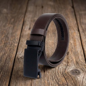 May include: A dark brown belt with a textured surface and a matte black rectangular buckle. The belt features a sliding ratchet mechanism on the underside of the strap, designed for a secure fit without traditional holes in the leather strap.