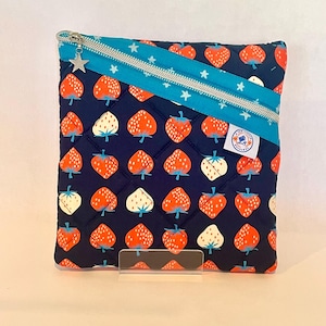May include: A quilted navy blue pouch with a repeating pattern of red and white strawberries. A turquoise zipper and accent band with silver stars and a star zipper pull add detail. A small patch is sewn on the side.