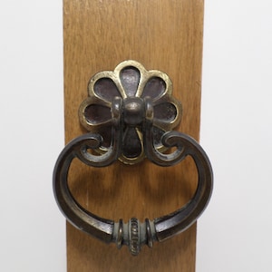 May include: A decorative door handle with a floral design. The handle is made of metal and has a dark brown finish. The handle is attached to a wooden door.