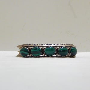 May include: A silver cuff bracelet featuring five large, round, polished malachite stones. The bracelet has an engraved design along the top edge and is set against a white background. The malachite stones are a deep green color.